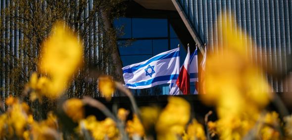 Polish and Israeli flags waving next to POLIN Museum building. In front of museum there is daffodil meadow.