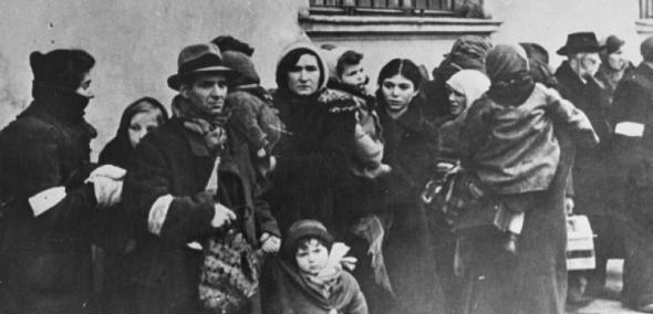Przy jakimś budynku stoją Żydzi z getta krakowskiego zgromadzeni przed deportacją. Zdjęcie czarno-białe.