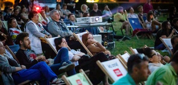 Widzowie kina letniego leżą na leżakach podczas seansu w ramach "POLIN na Łące".