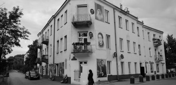 Czarno-białe zdjęcie kamienicy, na której ścianach namalowane są portrety Żydów pomordowanych w pogromie kieleckim w 1946 roku