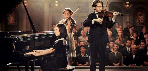 Cudowne dzieci (Wunderkind) - pokaz filmu w ramach WJFF, Na zdjęciu: kadr z filmu, przedstawia troje dzieci, które stoją na scenie i grają: dziewczynka na pianinie, chłopiec i druga dziewczynka na skrzypcach