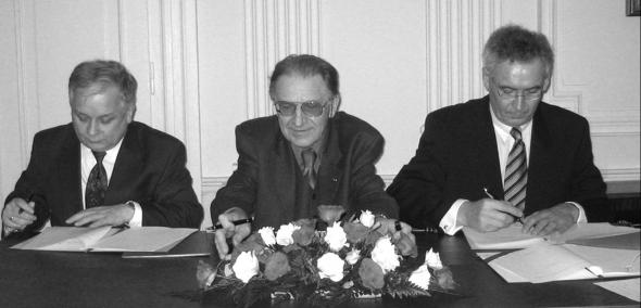 Lech Kaczyński przy wspólnym stole z dwoma innymi mężczyznami.