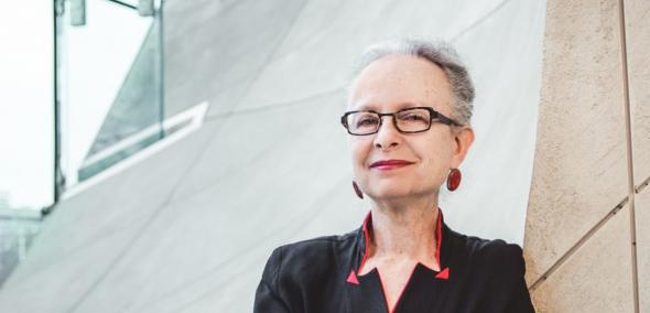 Prof. Barbara Kirshenblatt-Gimblett stoi oparta o ścianę muzeum w kolorze piasku pustyni