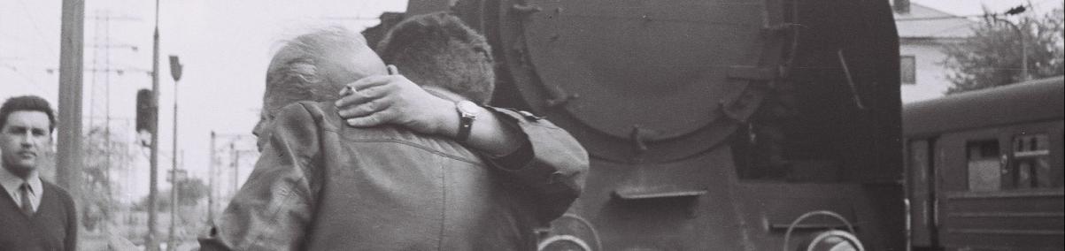 Zdjęcie archiwalne. Dwoje ludzi przytula się do siebie. W tle lokomotywa.
