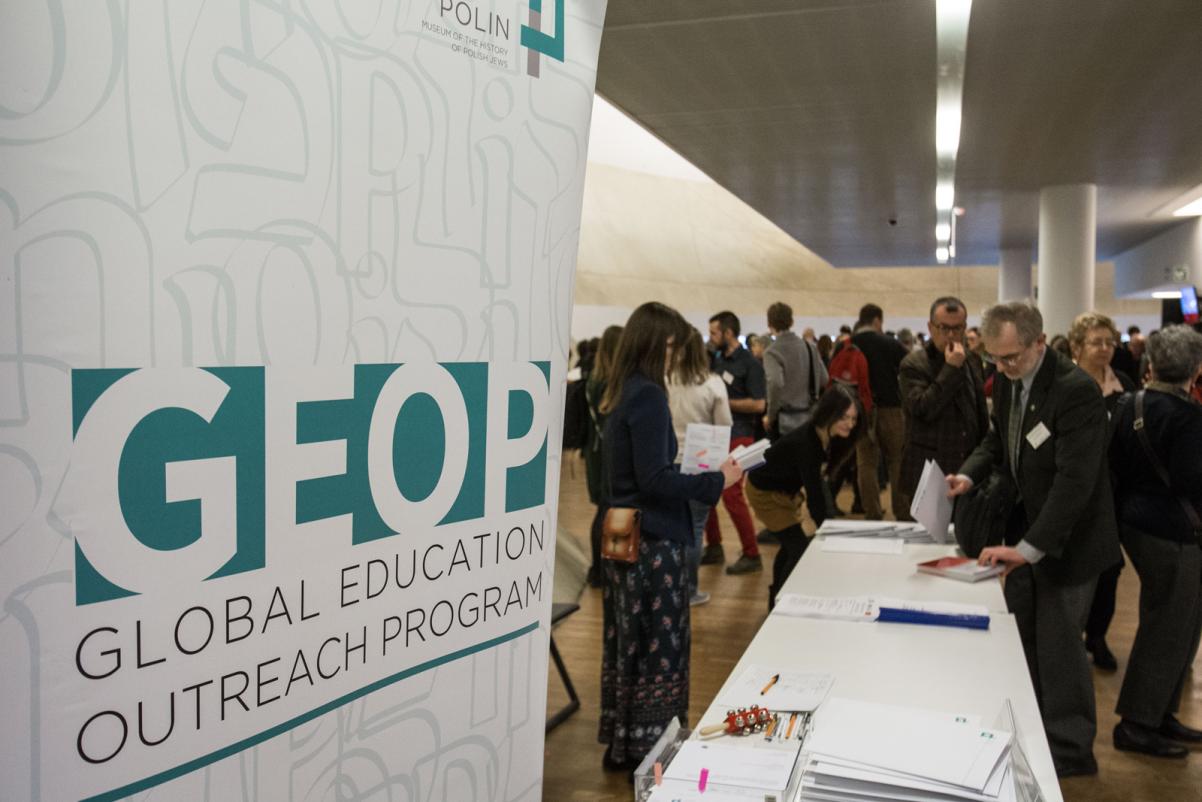 Na pierwszym planie baner reklamowy z napisem GEOP, Global Educational Outreach Program, w tle osoby rejestrujące się na konferencję