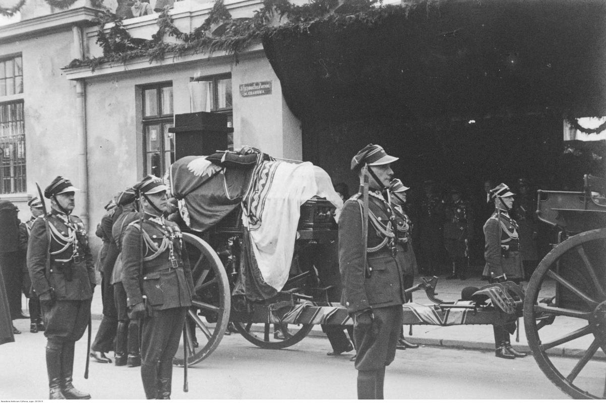 Zdjęcie archiwalne - żołnierze w mundurach galowych stoją na baczność wokół lawety. Na lawecie trumna z ciałem Józefa Piłsudskiego przykryta flagą Polski. Na trumnie leży czapka Piłsudskiego i jego szabla.