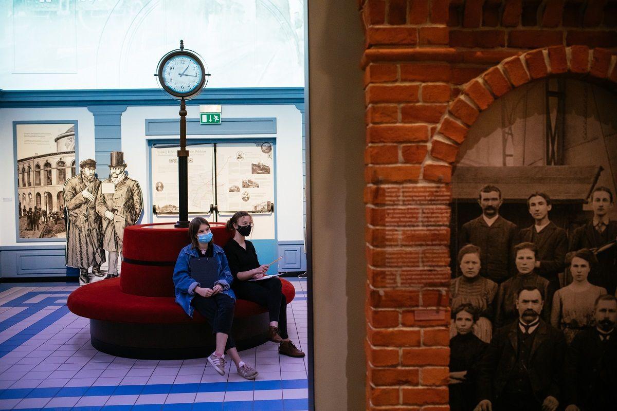 Dwie osoby siedza na kanapie na dworcu w przestrzeni wystawy stałej Muzeum POLIN