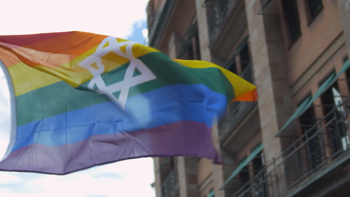 Na wietrze powiewa tęczowa flaga społeczności LGBT, na której narysowana jest też gwiazda Dawida.