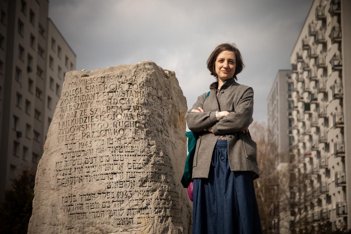Przewodniczka Julia Chimiak stoi obok kamienia-pomnika z wyrytymi nazwiskami.