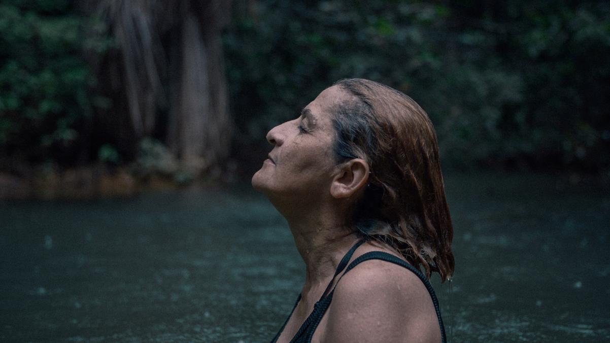 Kadr z filmu "Terytorium". Starsza kobieta stoi bokiem, unosząc lekko głowę. Otacza ją woda.