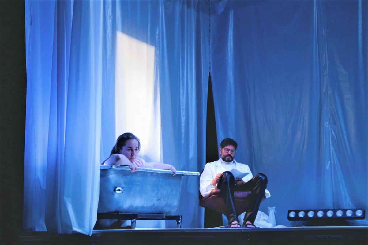 Kadr z czytania performatywnego "Sześć żeber gniewu" - dziewczyna siedzi w wannie, a obok niej na krześle mężczyzna.