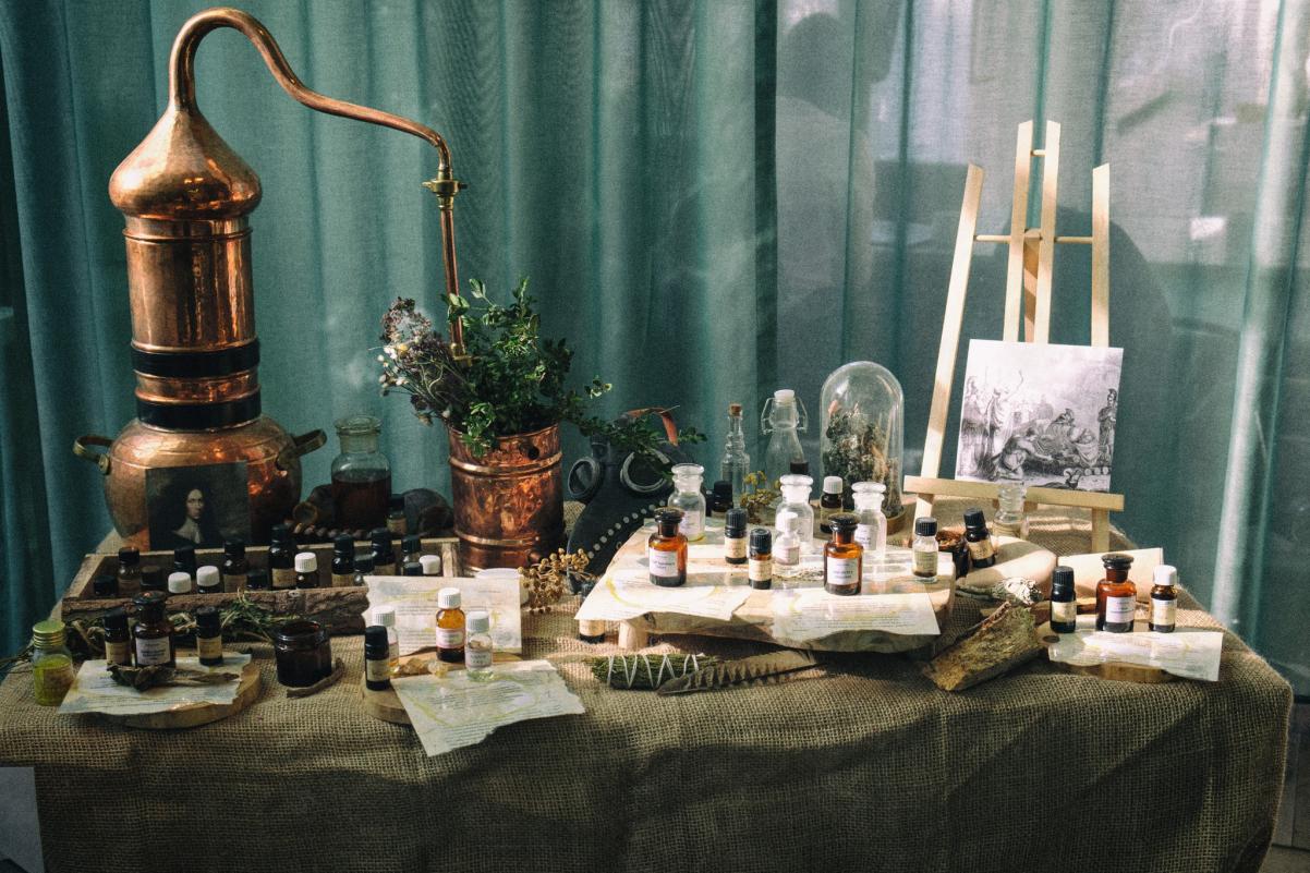 Instalacja zapachowa "Bottanicum" Moniki Opieki-Nowak - na stoliku stoją m.in. zapachy w buteleczkach, mała sztaluga z obrazkiem, roślinka w doniczka.