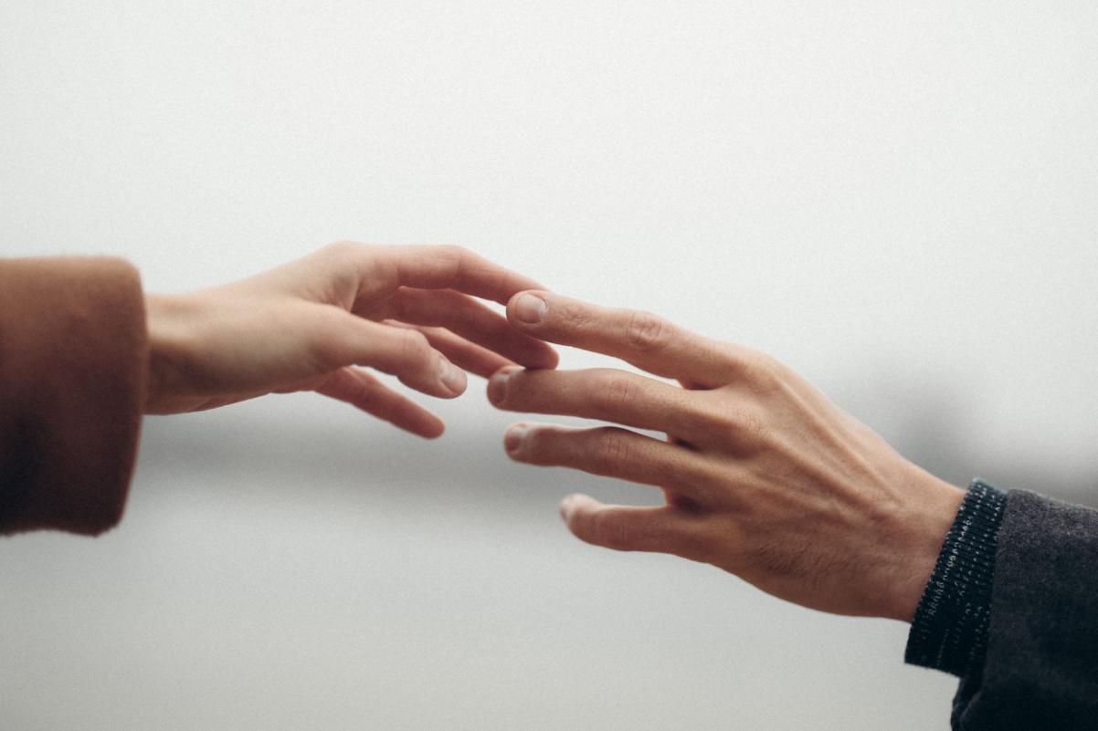 Dwie osoby wyciągają ku sobie dłonie i dotykają się opuszkami palców.