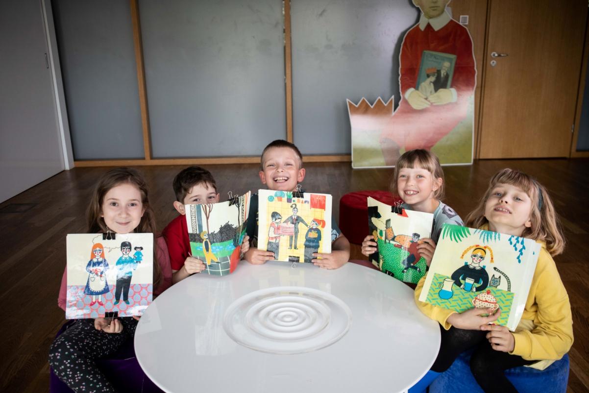 Pięcioro dzieci siedzi przy stoliku w sali edukacyjnej w Muzeum POLIN i trzyma przed sobą kolorowe obrazki.