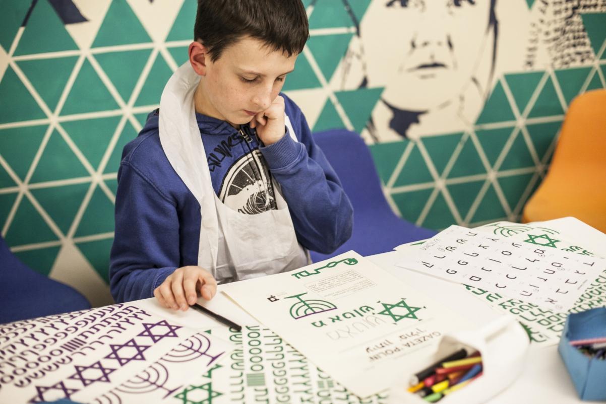 Warsztaty dla szkół w Muzeum POLIN. Na zdjęciu chłopiec pochylony nad kartką z treścią w języku hebrajskim. Zamyślony. Opiera głowę na ręce.