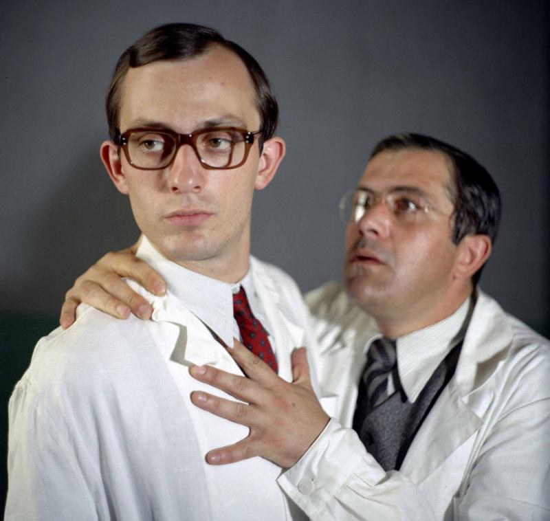 Kadr z filmu "Szpital przemienienia". Dwaj lekarze. Jeden z nich patrzy w bok, drugi spogląda na niego i trzyma dłoń na jego klatce.