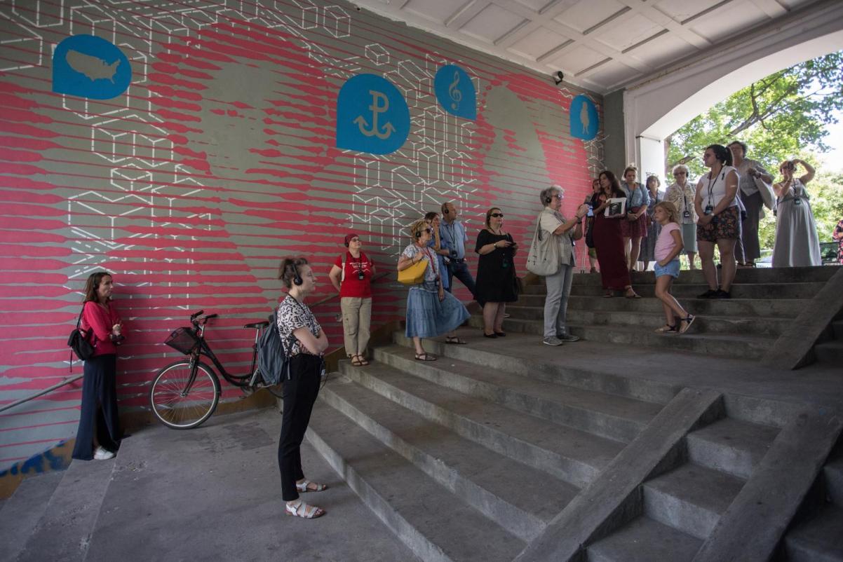Grupa ludzi podczas spaceru po Muranowie przy jednym z murali