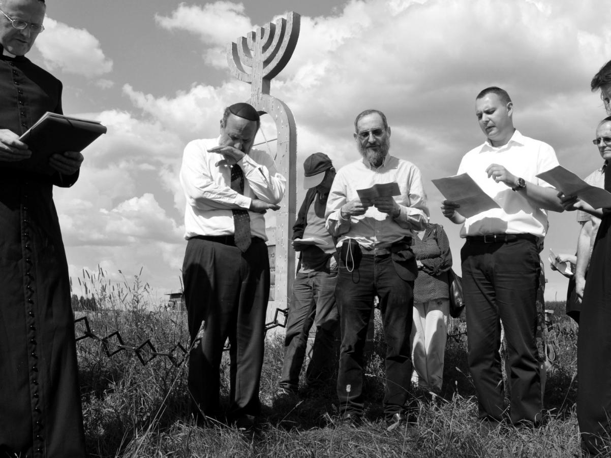 Czarno-biała fotografia przedstawia modlących się Żydów w miejscu pamięci.