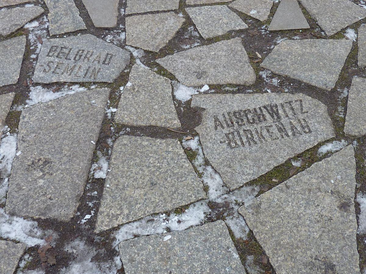 Płyty chodnikowe, dwie z nich mają napisy, jedna - Auschwitz-Birkenau, druga - Belgrad-Semlin.