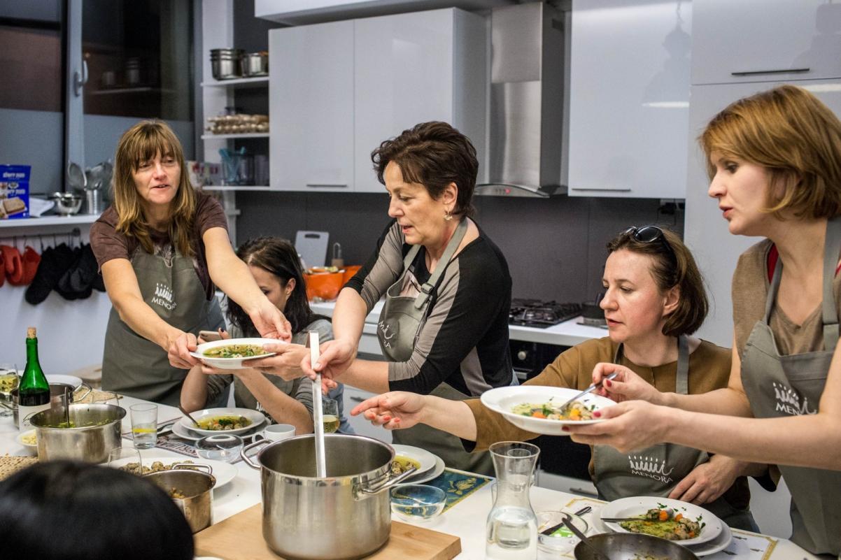 Grupa kobiet gotuje podczas warsztatów kulinarnych.