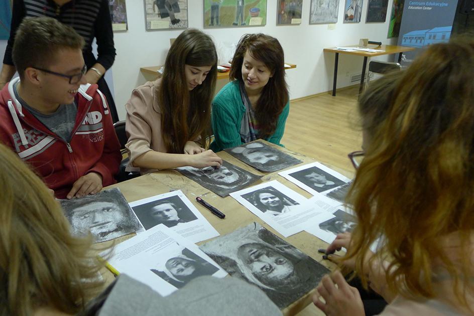 Kilka młodych osób ogląda zdjęcia ułożone na stole.