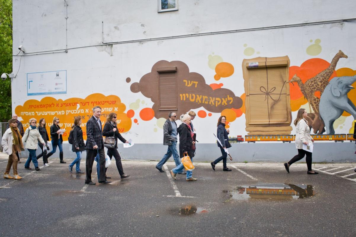 Grupa osób na spacerze po Warszawie. Grupa idzie przy muralu.