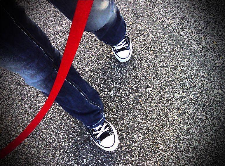 Jakaś osoba trzyma czerwony sznurek. Widać tylko jej nogi.