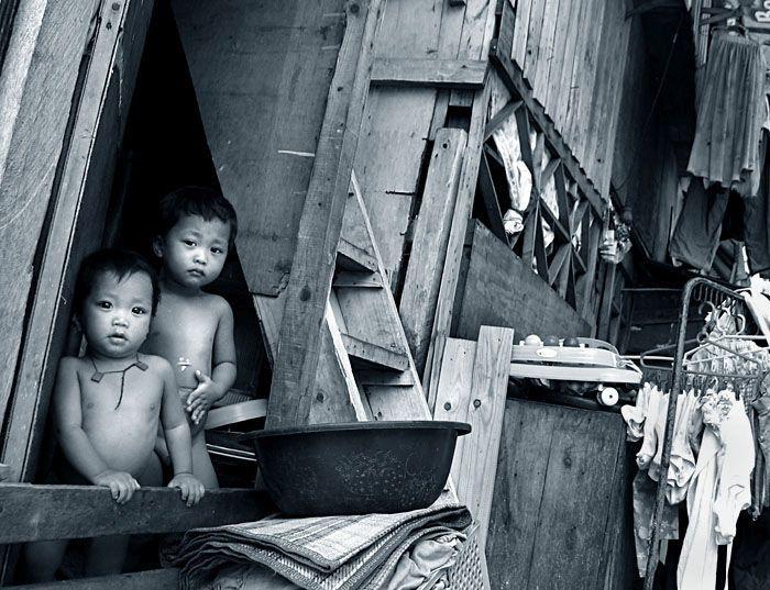 Czarno-białe zdjęcie przedstawia dwóch małych chłopców wyglądających z okienka.