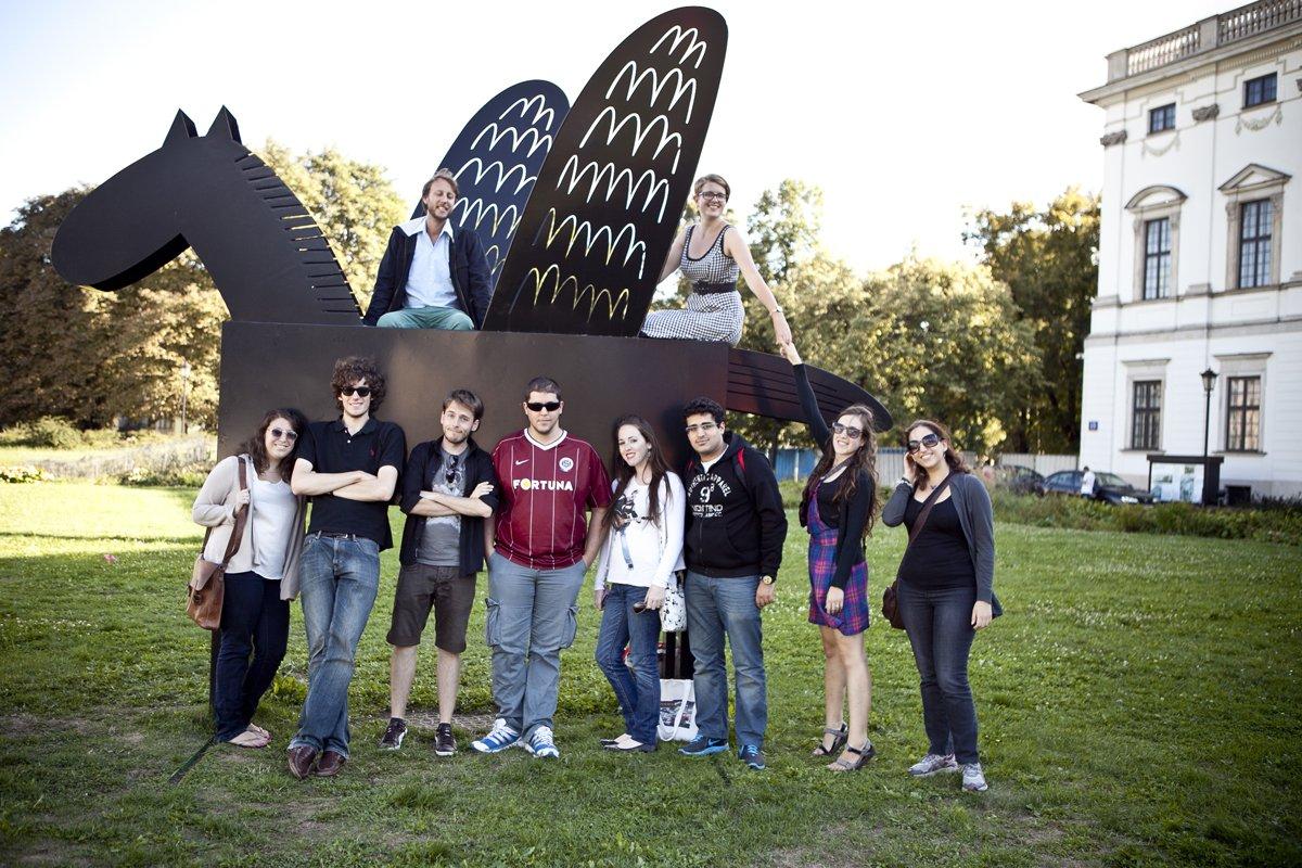 Grupa młodych osób przed budynkiem Biblioteki Narodowej i instalacji z pegazem.