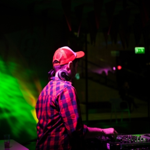 DJ w czapce z daszkiem stoi przy konsolecie.