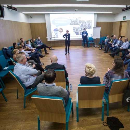 Grupa osób siedzi na krzesłach w sali konferencyjnej Muzeum POLIN. Przy rzutniku stoją dwie osoby prowadzące spotkanie.