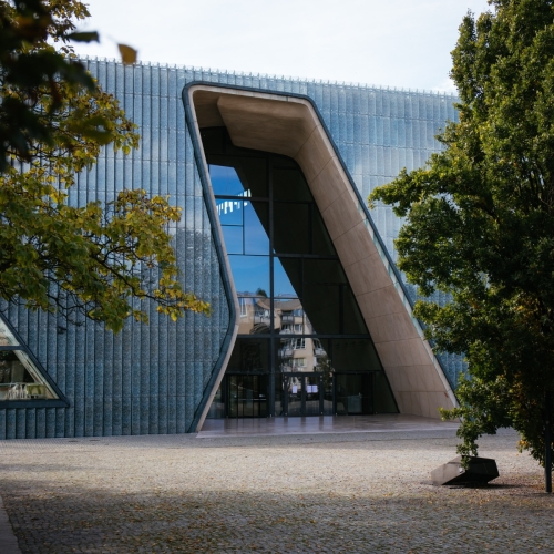 Budynek Muzeum POLIN wśród zielonych drzew.
