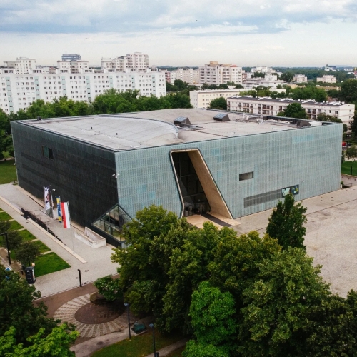 Budynek Muzeum POLIN z lotu ptaka. Otoczony zielonymi drzewami i blokami na Muranowie.
