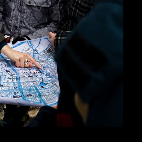 Kilka osób trzyma mapę Muranowa. Ktoś wskazuje jakiś punkt na mapie.