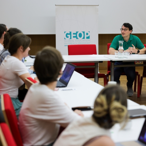Prowadzący i uczestniczki Szkoły letniej siedzą przy stole w sali konferencyjnej.