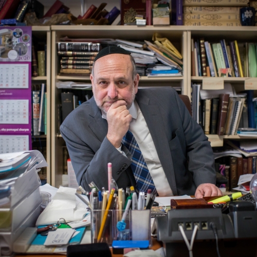 Rabin Michael Schudrich siedzi przy biurku w gabinecie. Za nim regały wypełnione książkami.