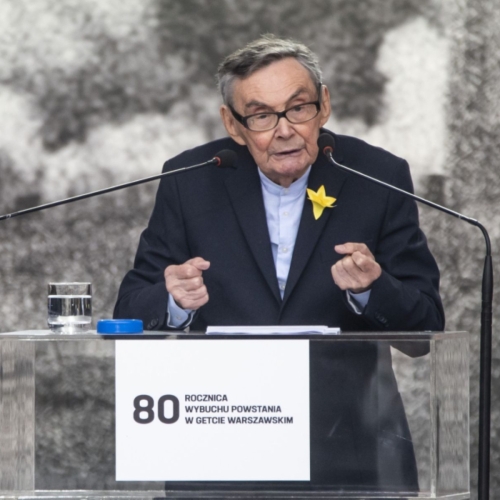 Marian Turski wygłasza przemówienie podczas obchodów 80. rocznicy powstania w getcie warszawskim. Stoi przy pulpicie mównicy, na której naklejona jest tabliczka z napisem "80 rocznica powstania w getcie warszawskim".