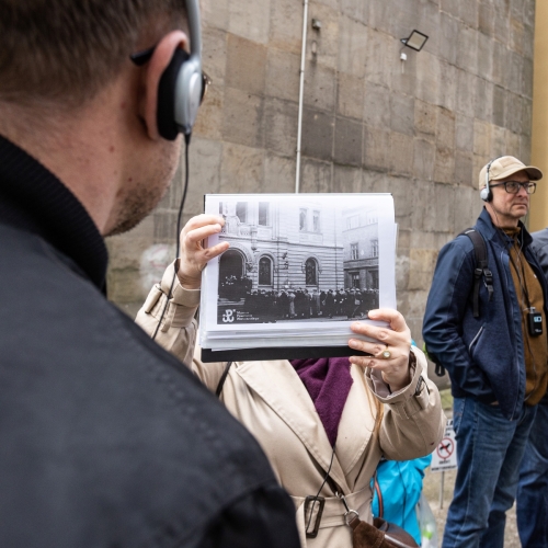 Przewodniczka pokazuje grupie archiwalne zdjęcie budynku podczas spaceru miejskiego po Warszawie.